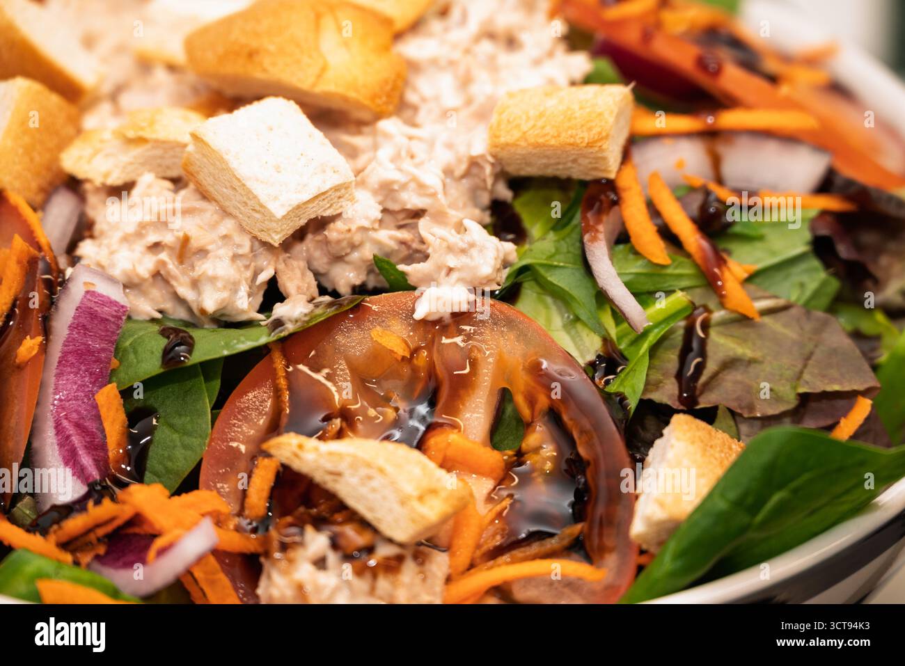 Lo chef prepara un'insalata di panzanella con pomodori, verdure, tonno, crostini, carote, e condimento balsamico per un pranzo leggero. Foto Stock
