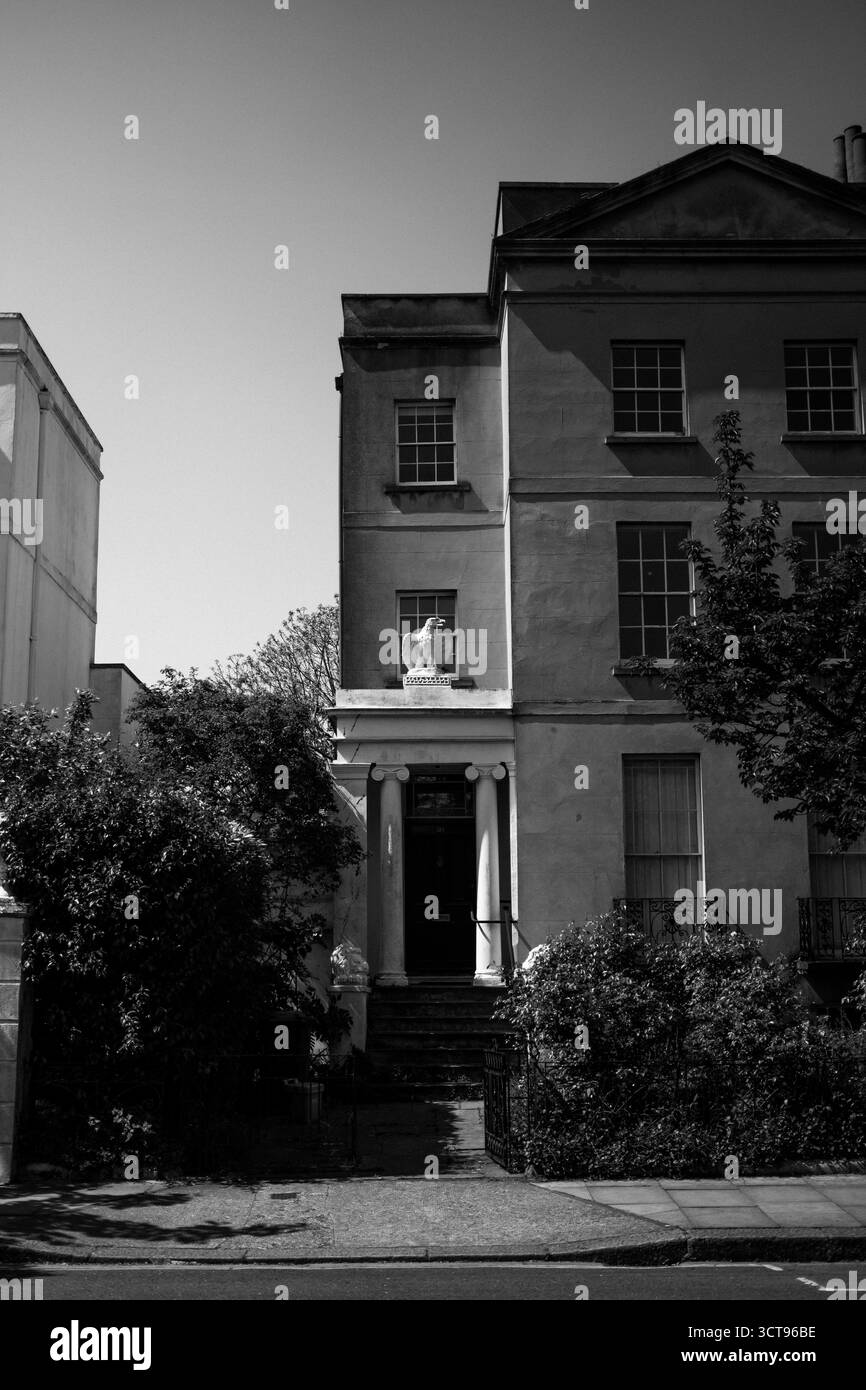 Chiswick, Londra – 2025.04.28 – foto in bianco e nero di una casa in stile georgiano con colonne e una porta scura, circondata da alberi e fogliame Foto Stock
