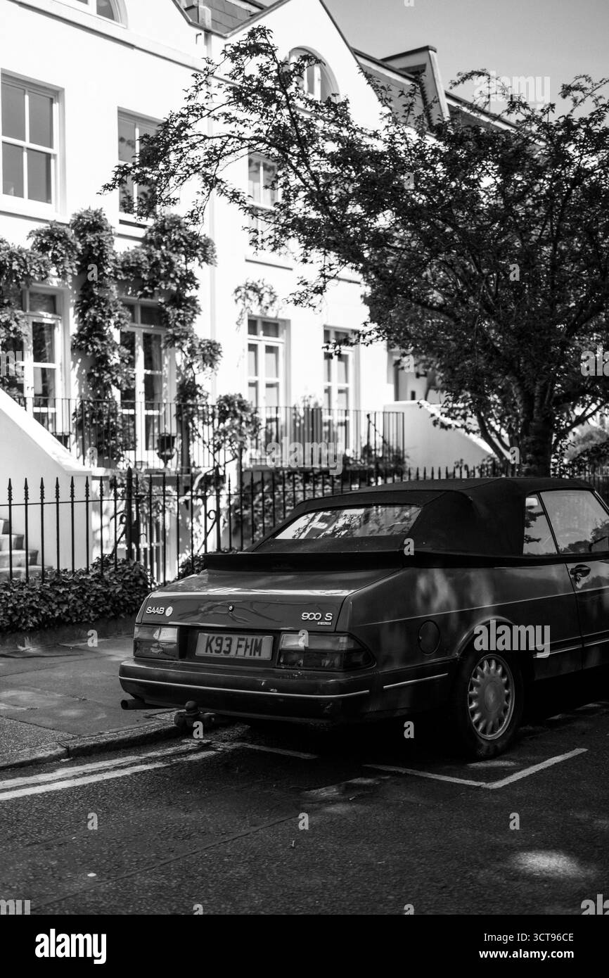 Chiswick, Londra – 2025.04.28 – foto in bianco e nero di una Saab 900S decappottabile d'epoca parcheggiata in una tranquilla strada residenziale con case a schiera bianche Foto Stock