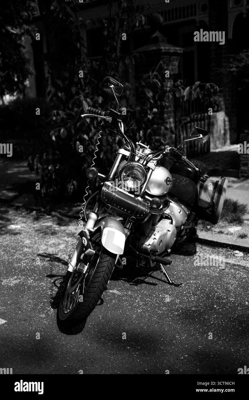 Chiswick, Londra – 2025.04.28 – Una motocicletta classica con dettagli cromati si erge all'ombra di un albero lungo una tranquilla strada residenziale, captur Foto Stock