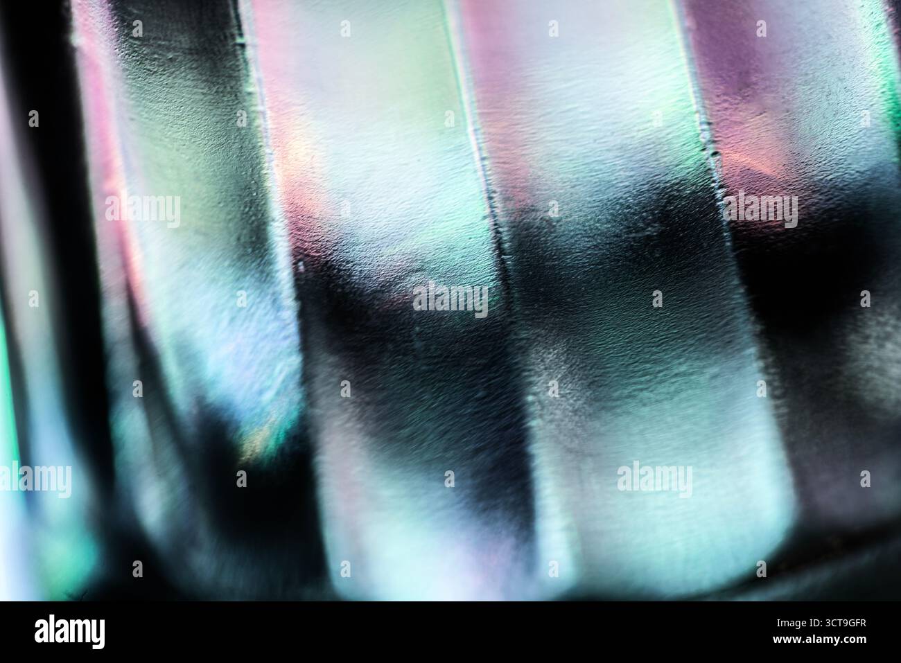 Primo piano astratto della superficie in vetro testurizzato con rilievi lisci, che riflettono sfumature delicate di luce verde, blu, viola e rosa, creando un iridescente, m Foto Stock