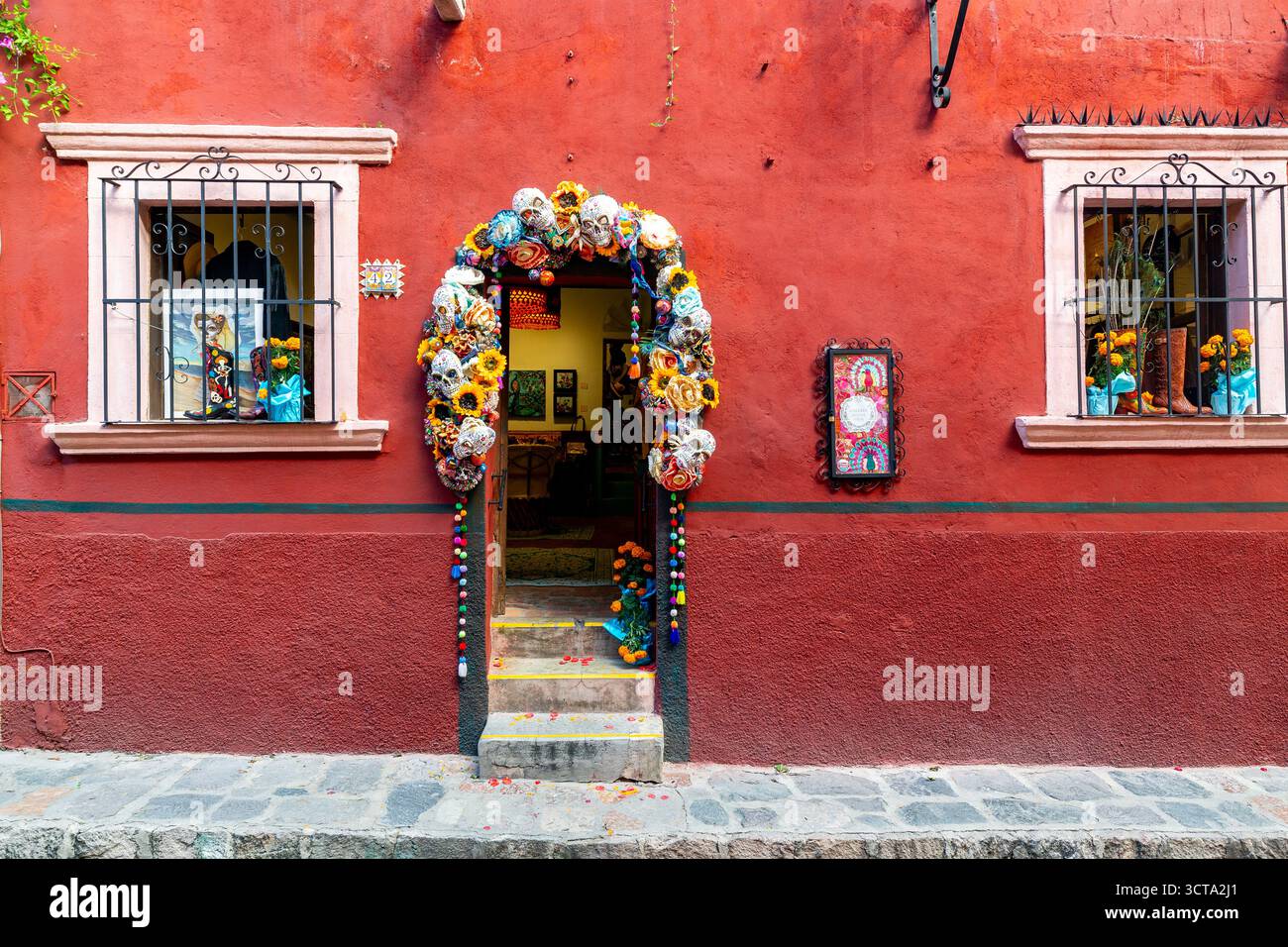 L'ingresso di un edificio è decorato con teschi e fiori, probabilmente per celebrare il giorno dei morti. L'edificio e' dipinto di rosso vibrante. Foto Stock