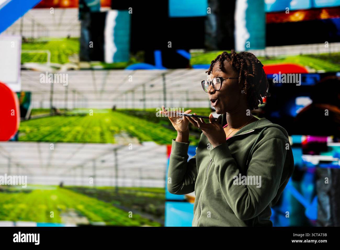 Giovane donna che usa il microfono del telefono per inviare messaggi audio sul consumo di contenuti multimediali condivisi e sullo sfondo multimediale colorato. Una donna afroamericana parla sullo smartphone per condividere opinioni sui video online Foto Stock