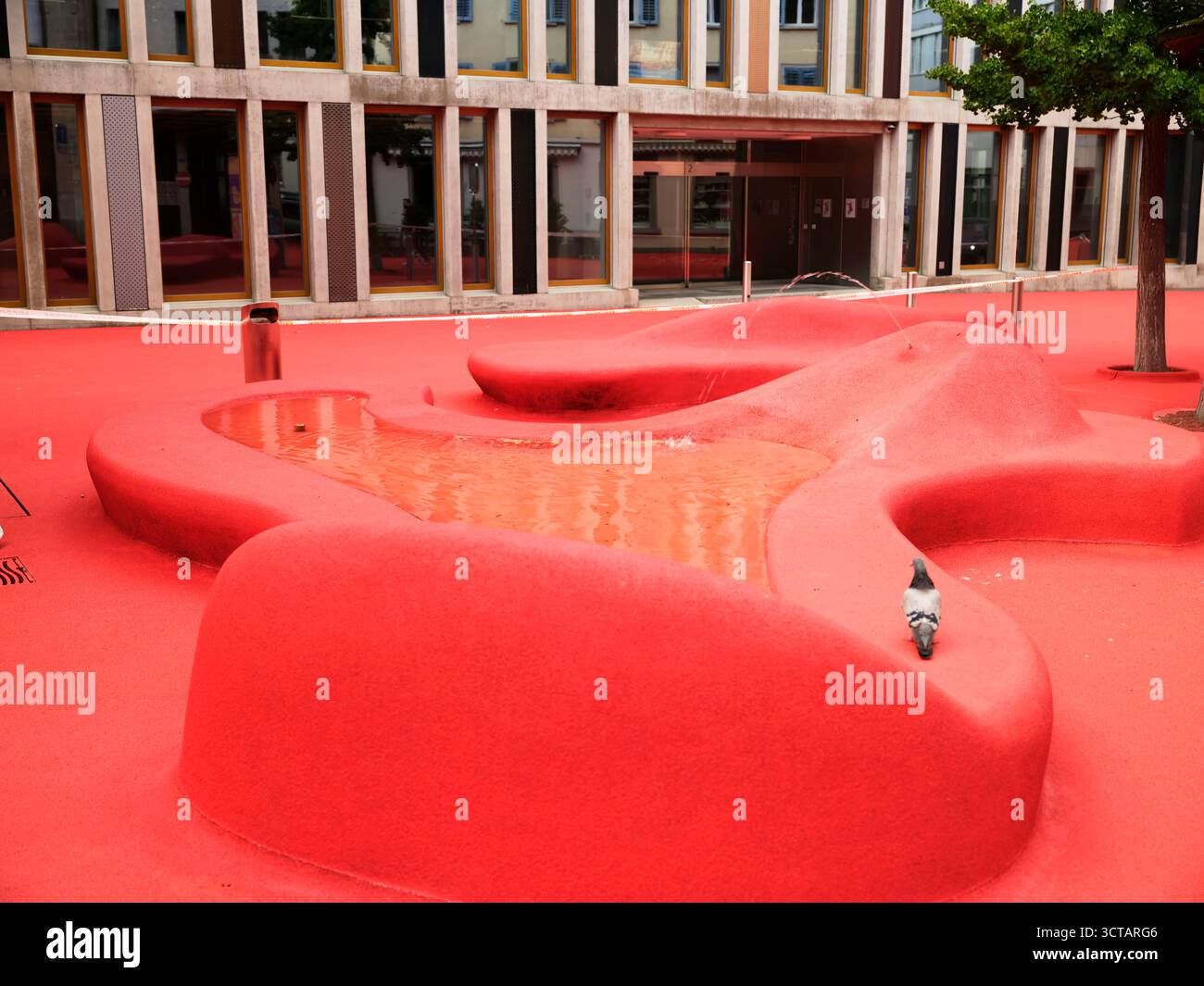 Paesaggio rosso unico con laghetto e strutture artistiche in un parco urbano in una giornata di sole Foto Stock