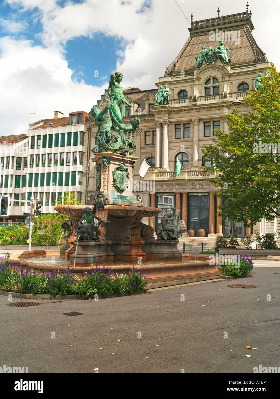 Elegante fontana in una vivace piazza della città circondata da architettura storica e vegetazione durante una giornata di sole Foto Stock