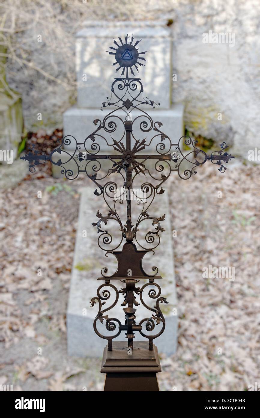 Croce di pietra in acciaio, forgiata e lucidata, sullo sfondo di una tomba in un cimitero autunnale Foto Stock
