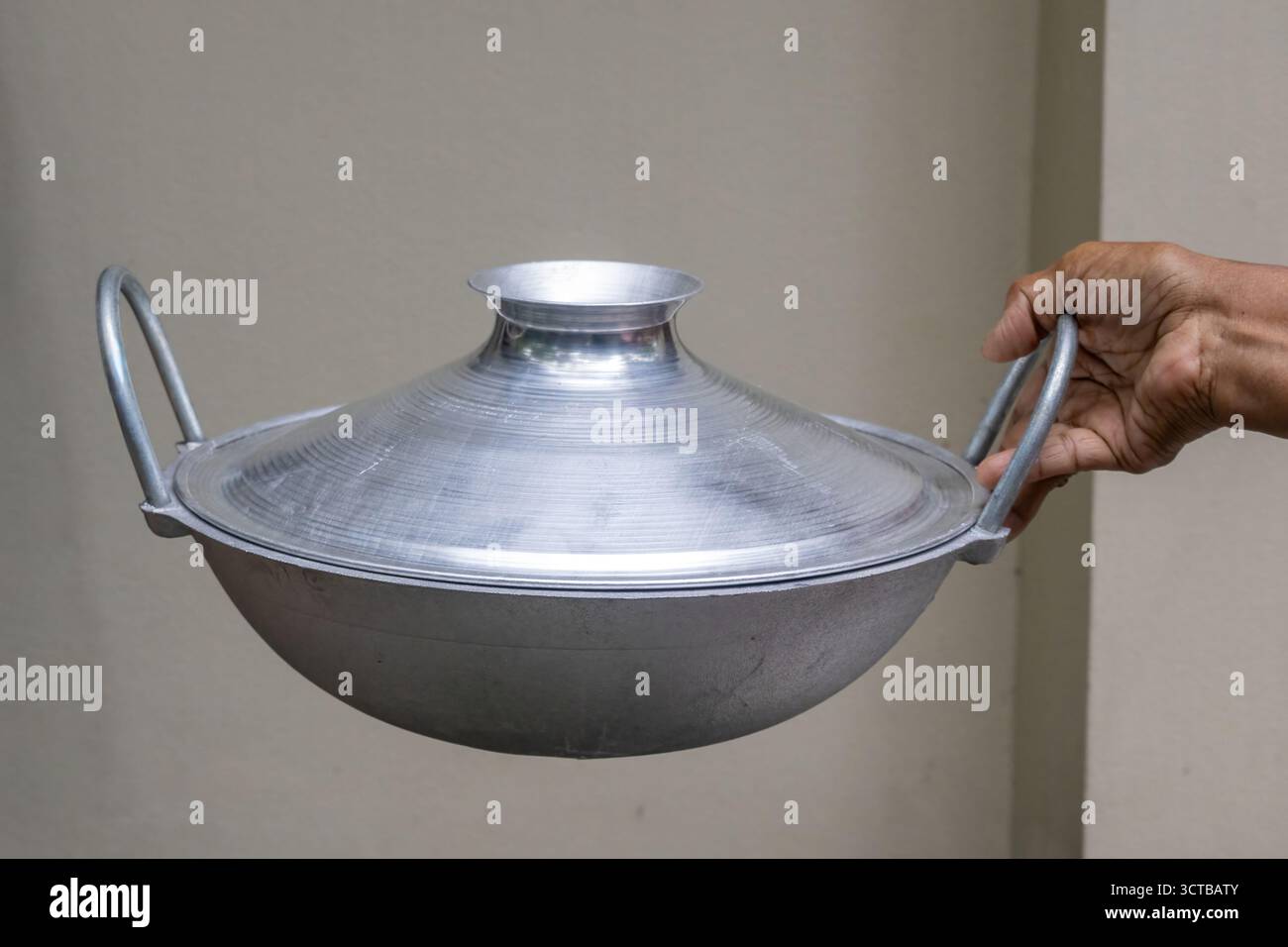 Mano che tiene in mano un tradizionale Kadai d'argento (chiamato anche Karahi o Kadhai) con una copertina coordinata. Questo piatto da cucina profondo e circolare usato per l'indiano e il Bang Foto Stock