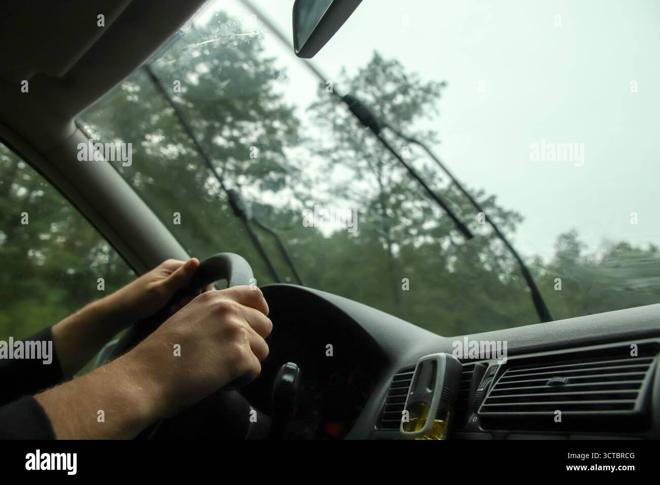 pioggia, concentrandosi sulla visuale dall'interno del parabrezza dell'auto mentre il tergicristallo si muove. il conducente può vedere i vetri del traffico di giorno piovoso. tergicristalli su parabrezza traffico umido. Foto Stock