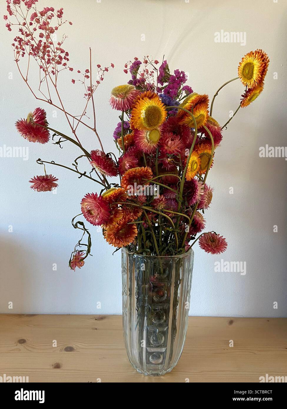 Un morbido bouquet di fiori secchi gialli, rossi, arancioni e viola in un vaso di vetro vintage aggiunge un fascino caldo e rustico a un tavolo di legno. - Immagine stock catturata con smartphone