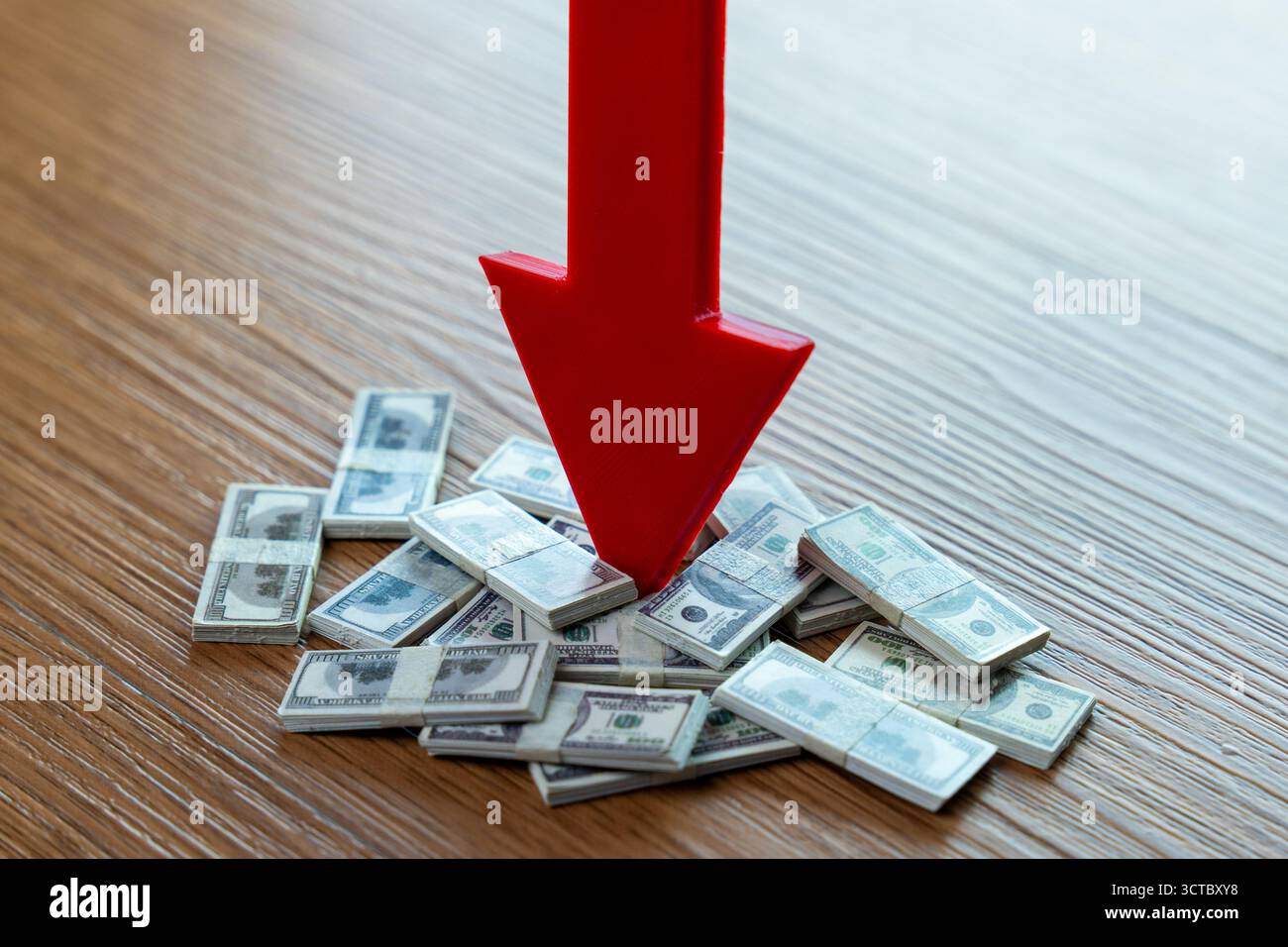 Freccia rossa verso il basso che indica pile di banconote in dollari statunitensi su una superficie in legno, che rappresenta una perdita finanziaria, un deprezzamento del dollaro e una contrazione della recessione economica Foto Stock