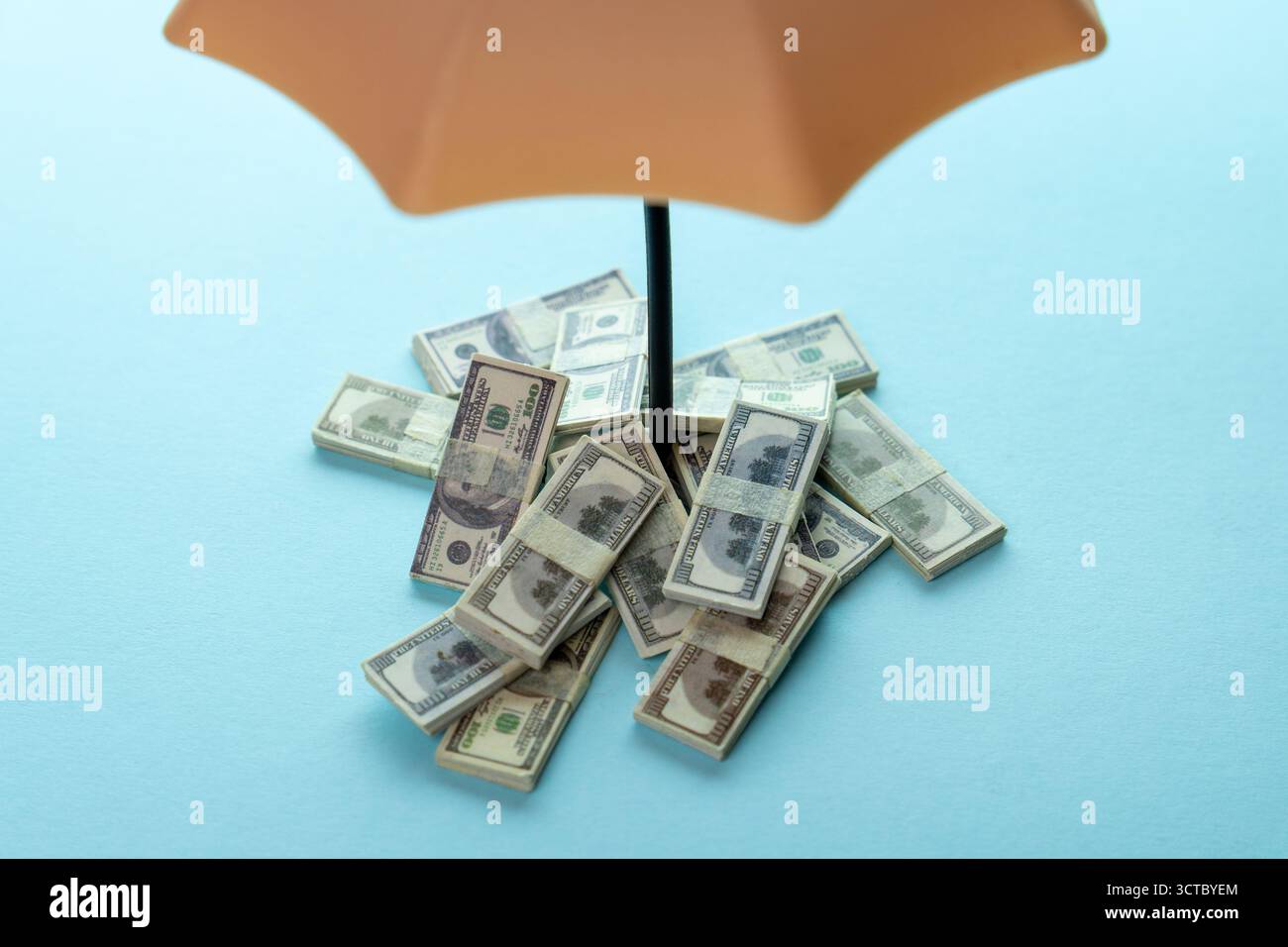 Pile di banconote in dollari USA sotto un ombrello su sfondo blu, simboleggiano la protezione finanziaria, la sicurezza dei risparmi e il concetto di sicurezza degli investimenti. Foto Stock