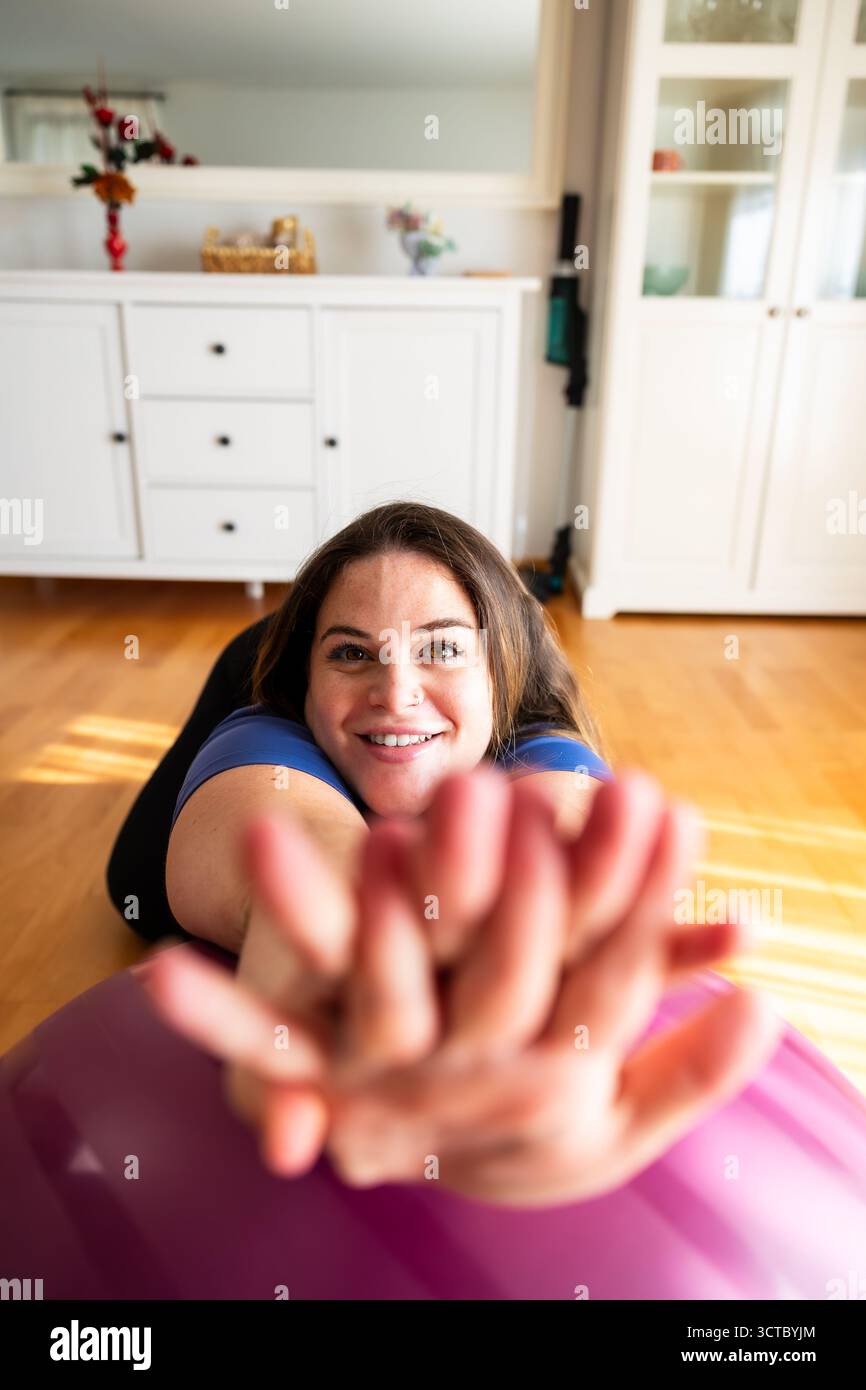 Donna sorridente incinta che si allunga sopra la palla fitness durante l'allenamento a casa. Stile di vita. Gravidanza. Foto Stock