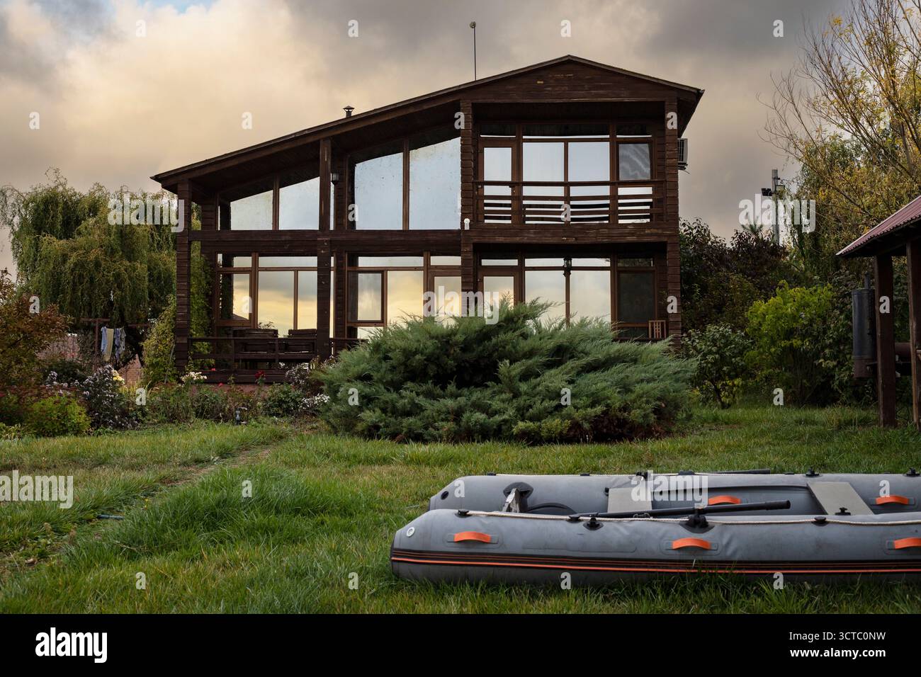 Moderna casa in legno con facciata in vetro e barca gonfiabile su erba verde. Concetto di vita ecologica, vacanza e relax nella natura. Foto Stock