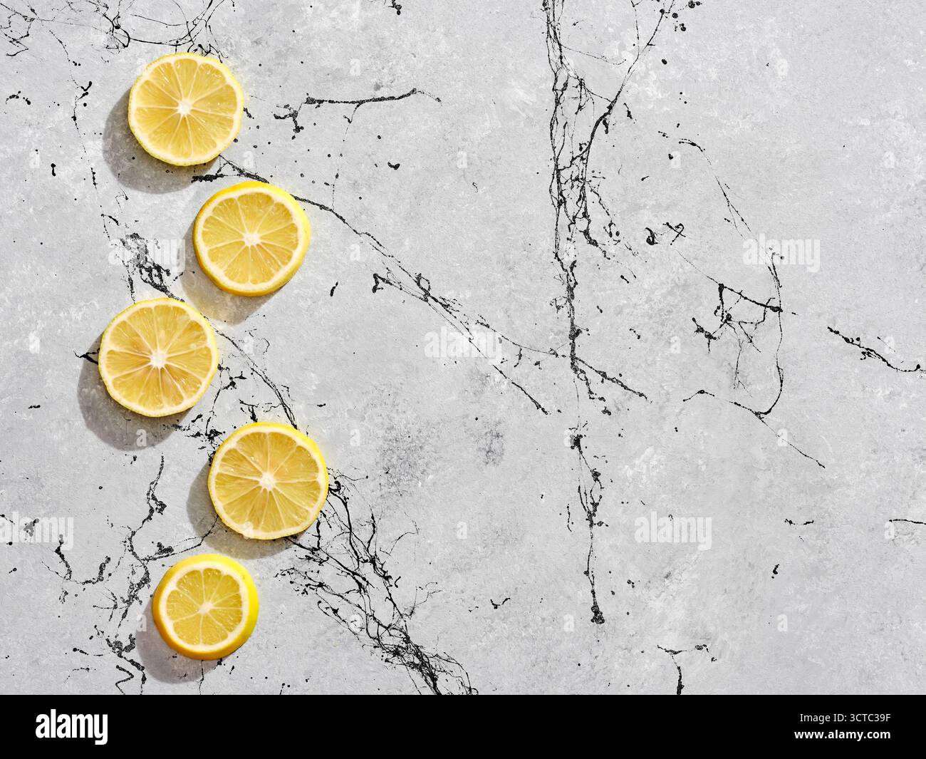 Linea verticale di fette di limone giallo fresco su sfondo di marmo grigio con venature nere, per un contrasto vibrante Foto Stock