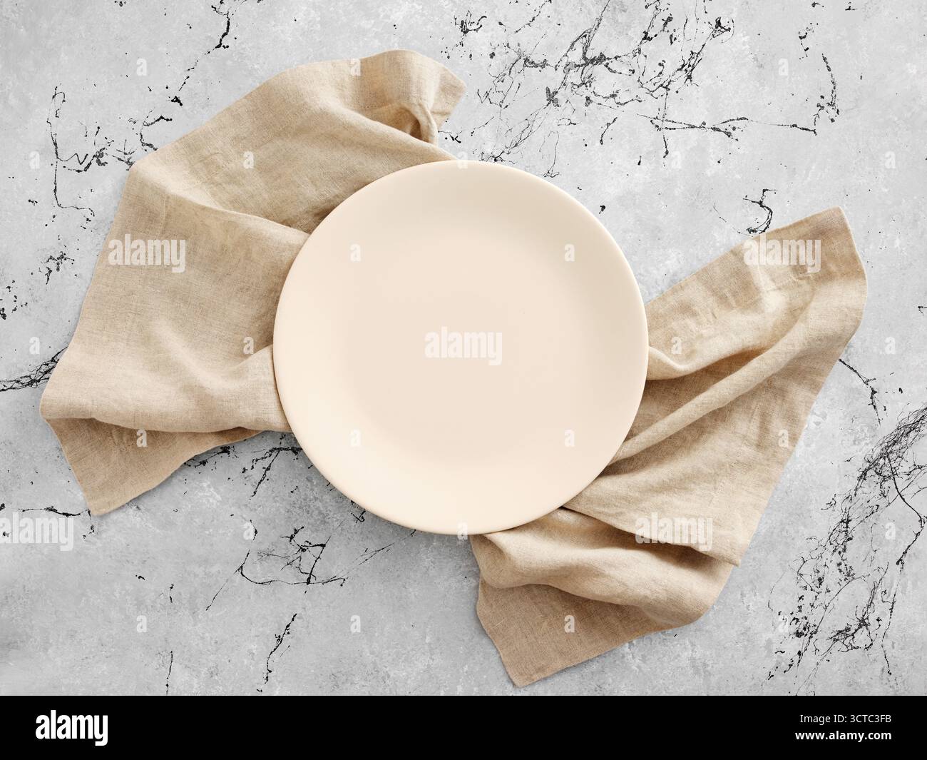 Piatto beige vuoto su un tovagliolo di lino naturale, appoggiato su uno sfondo di marmo grigio. Vista dall'alto che presenta lo spazio di copia. Impostazione del tavolo per il mockup dei cibi. Foto Stock