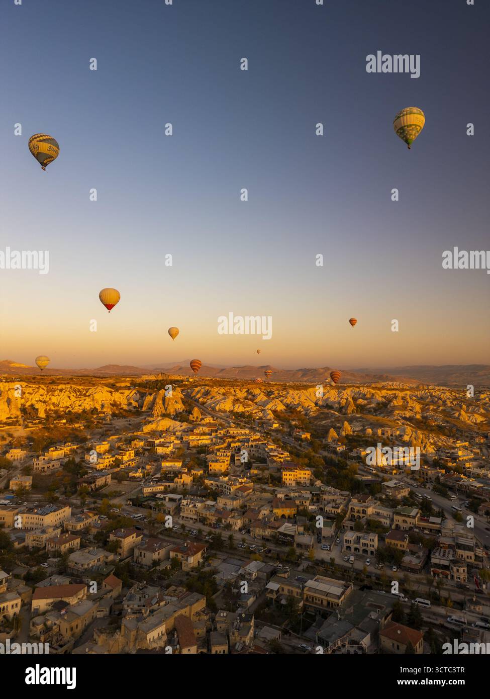Vista aerea delle mongolfiere che fluttuano serenamente sopra l'antico paesaggio mentre il sole che sorge getta un caldo bagliore sulle formazioni rocciose uniche, Goreme, Nevsehir e Turkiye. Foto Stock