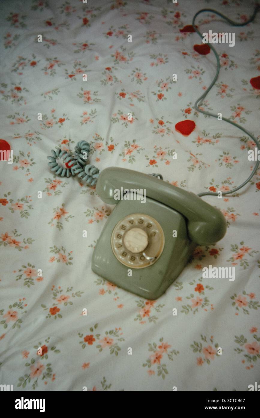 Un telefono rotativo vintage poggia su un copriletto floreale Foto Stock