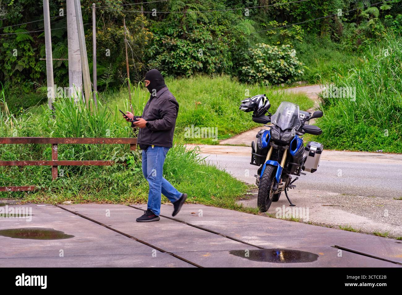 Un uomo che indossa una giacca nera e una copertura per il viso con la sua moto Foto Stock