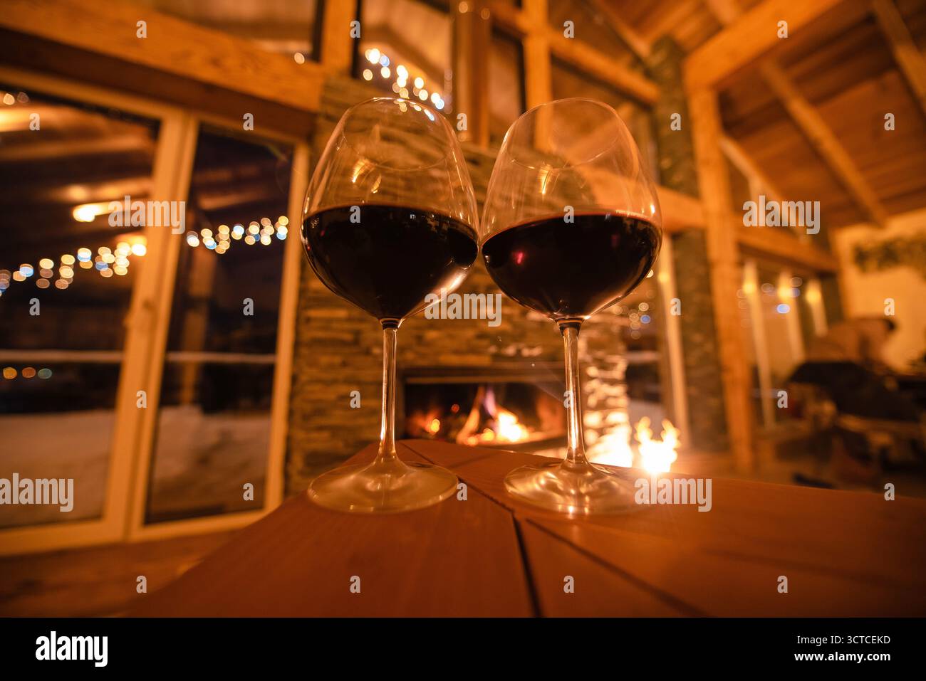 Serata accogliente in cabina con vino rosso accanto al caminetto Foto Stock