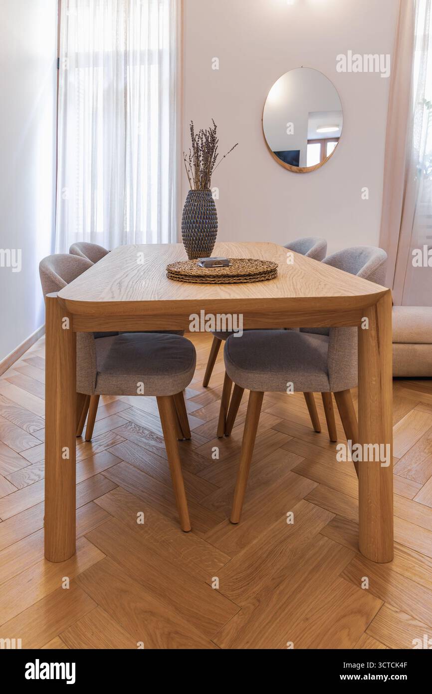 Еру tavolo da pranzo in legno e sedie in tessuto in un piccolo appartamento interno. Pavimento in parquet a spina di pesce e decorazioni in lavanda in tonalità neutre Foto Stock