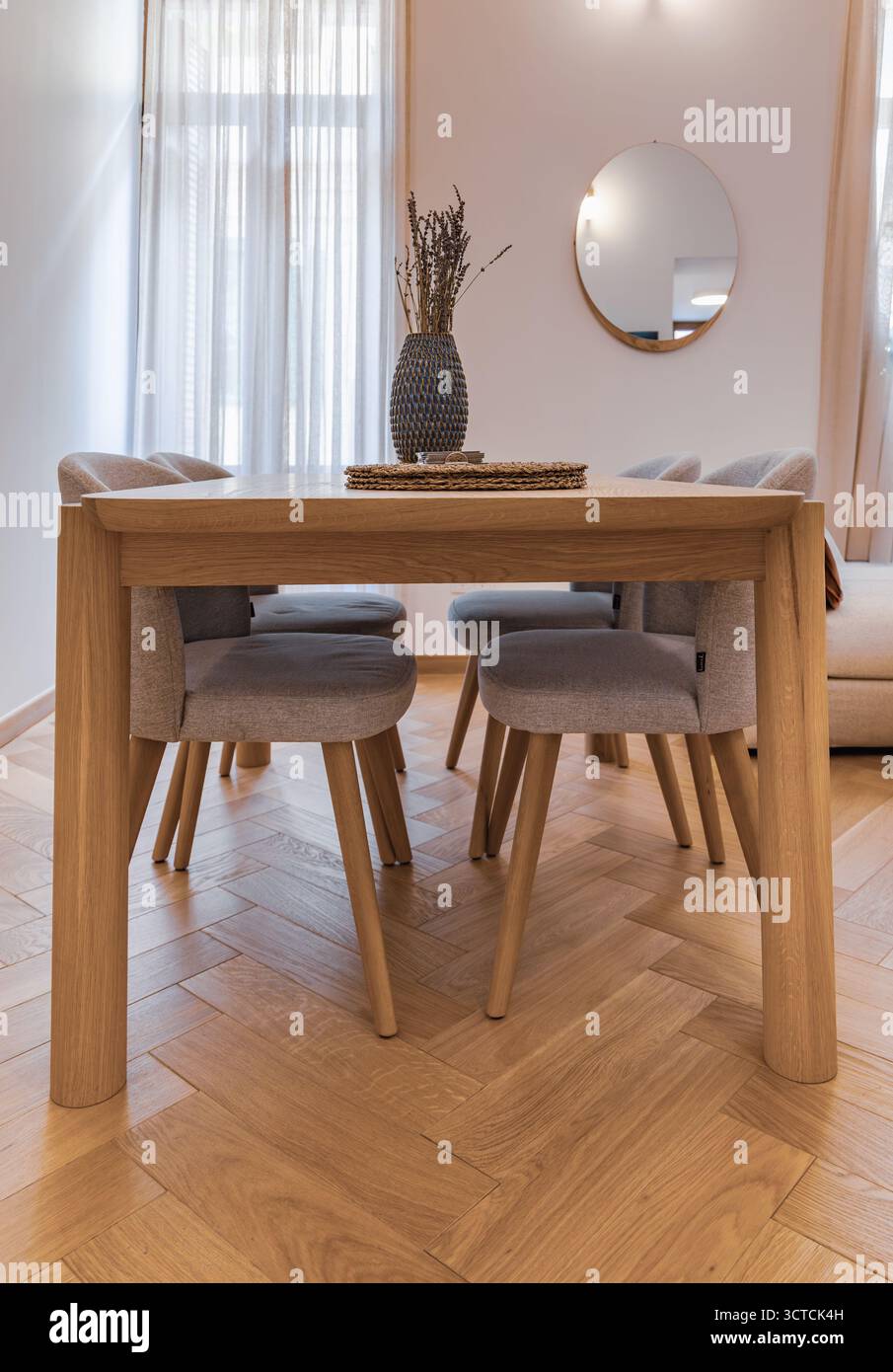 Еру tavolo da pranzo in legno e sedie in tessuto in un piccolo appartamento interno. Pavimento in parquet a spina di pesce e decorazioni in lavanda in tonalità neutre Foto Stock