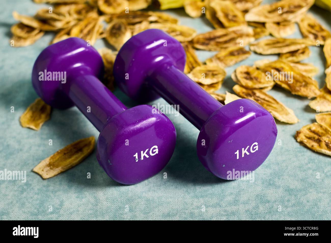 Immagine concettuale di scelte sane: Manubri viola e patatine di banana, che dimostrano l'equilibrio tra esercizio fisico e dieta per il benessere Foto Stock