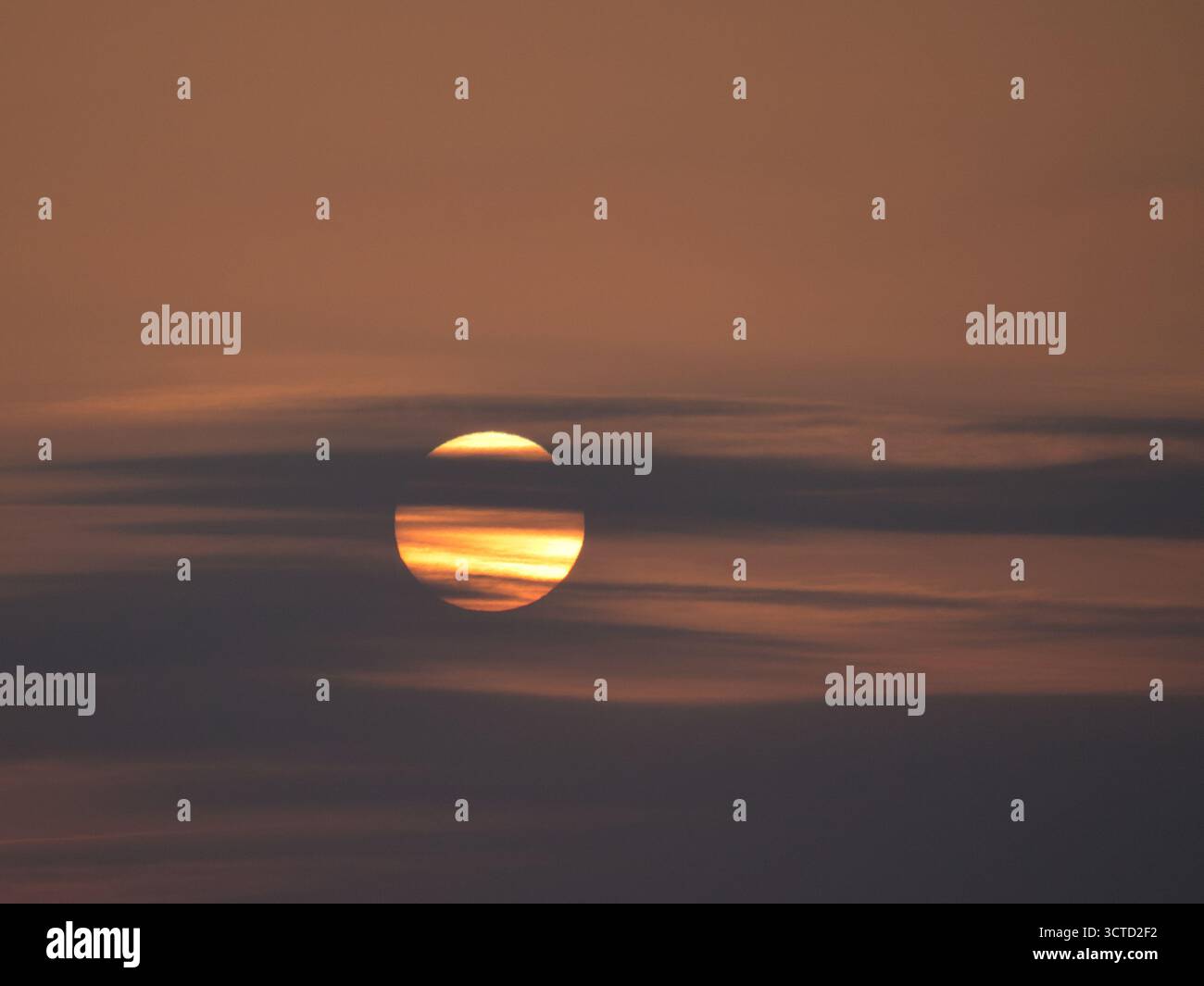 Tramonto ravvicinato attraverso gli impressionanti strati nuvolosi - primo piano del vibrante sole che tramonta parzialmente oscurato da nuvole orizzontali e fumose, creando Foto Stock