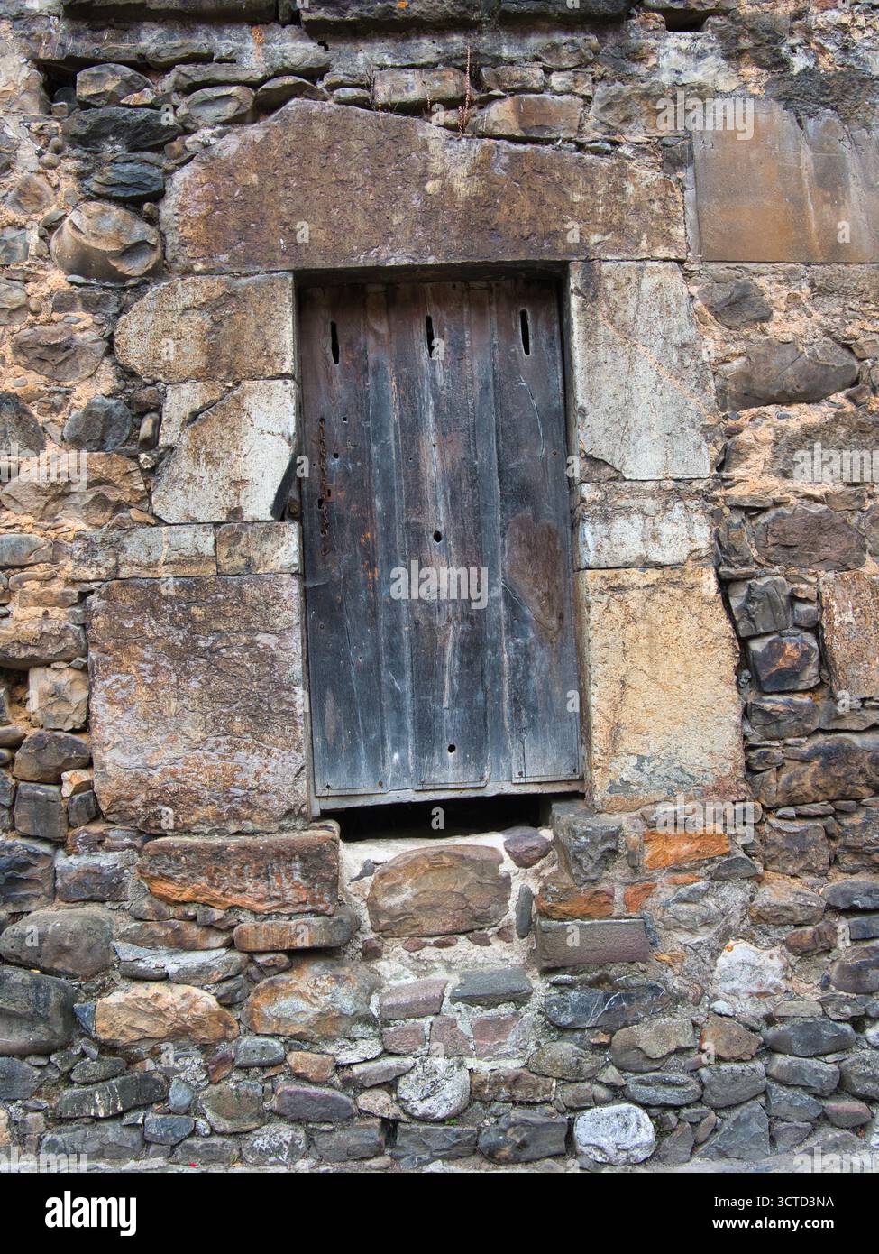 Muro in pietra rustico con finestra in legno antico - struttura muraria in pietra con struttura chiusa, rustica e danneggiata della finestra e persiane in legno. Trad Foto Stock