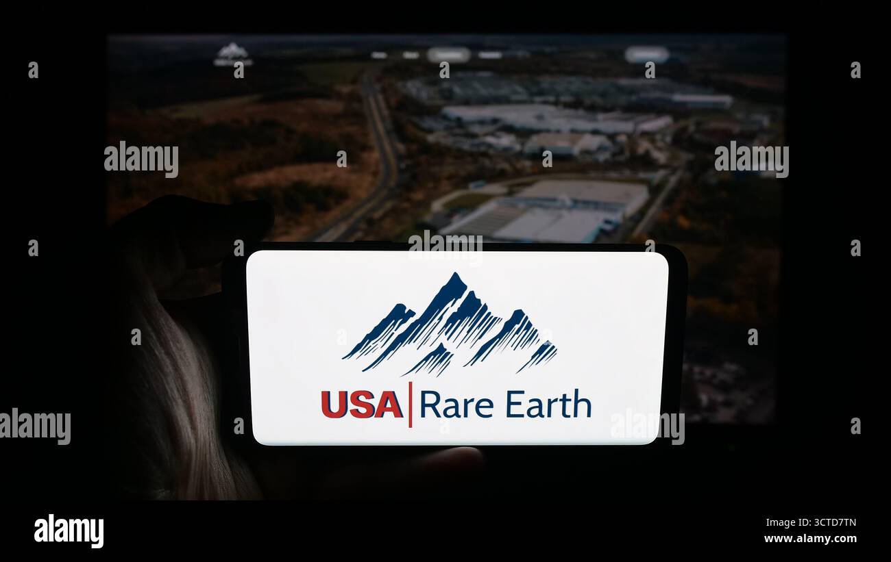 Stoccarda, Germania - 10-04-2025: Persona che tiene il cellulare con il logo della società mineraria USA rare Earth Inc. Sullo schermo davanti alla pagina web. Foto Stock