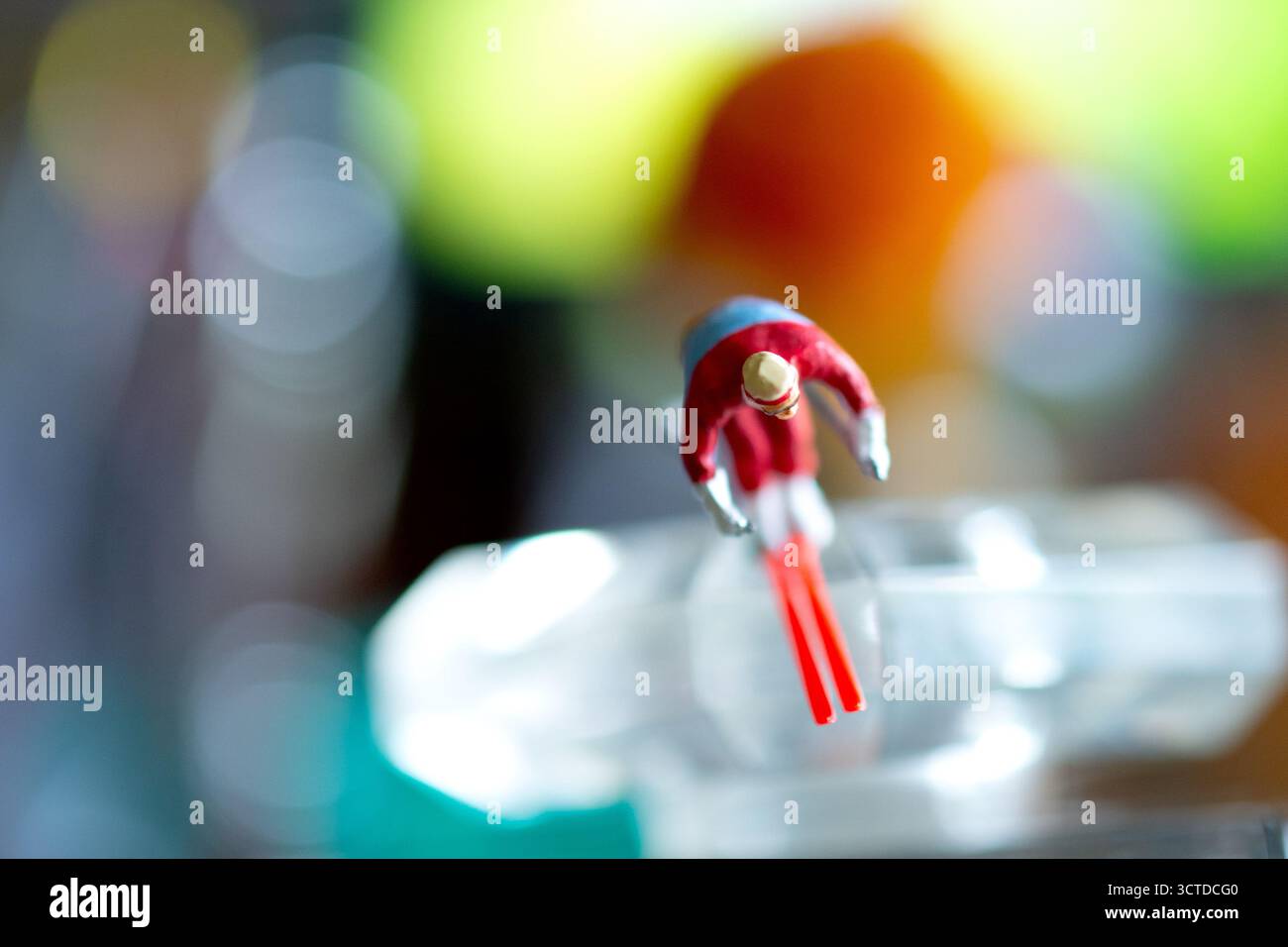 Una figura sciatrice in miniatura a metà salto sembra volare attraverso uno sfondo colorato e astratto, creando una scena surreale e dinamica. Foto Stock
