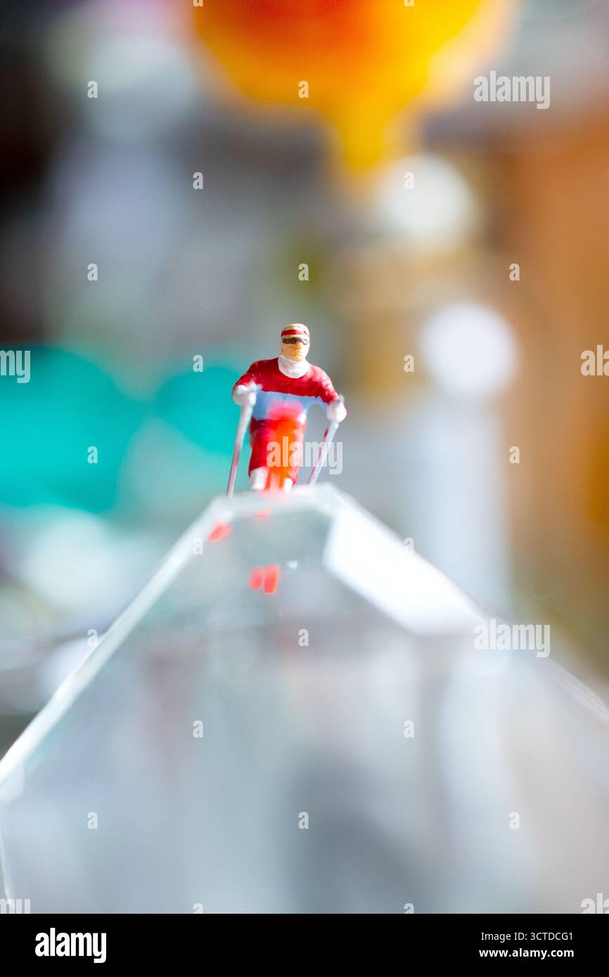 Una figura sciatrice in miniatura a metà salto sembra volare attraverso uno sfondo colorato e astratto, creando una scena surreale e dinamica. Foto Stock