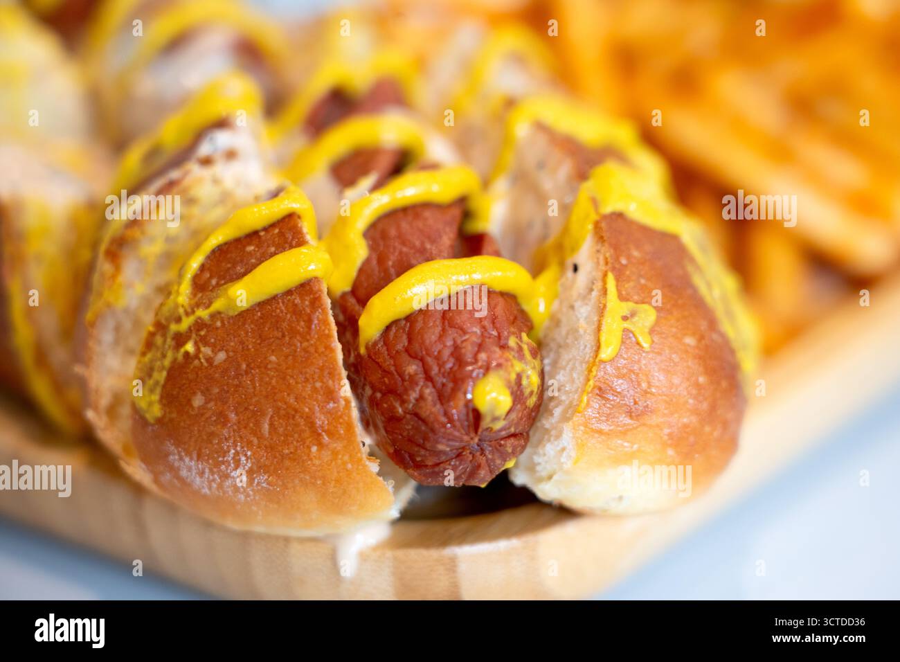 Hot dog caricati in soffici panini di pretzel con condimenti vivaci, serviti insieme a patatine fritte dorate per un pasto perfetto e appagante. Foto Stock