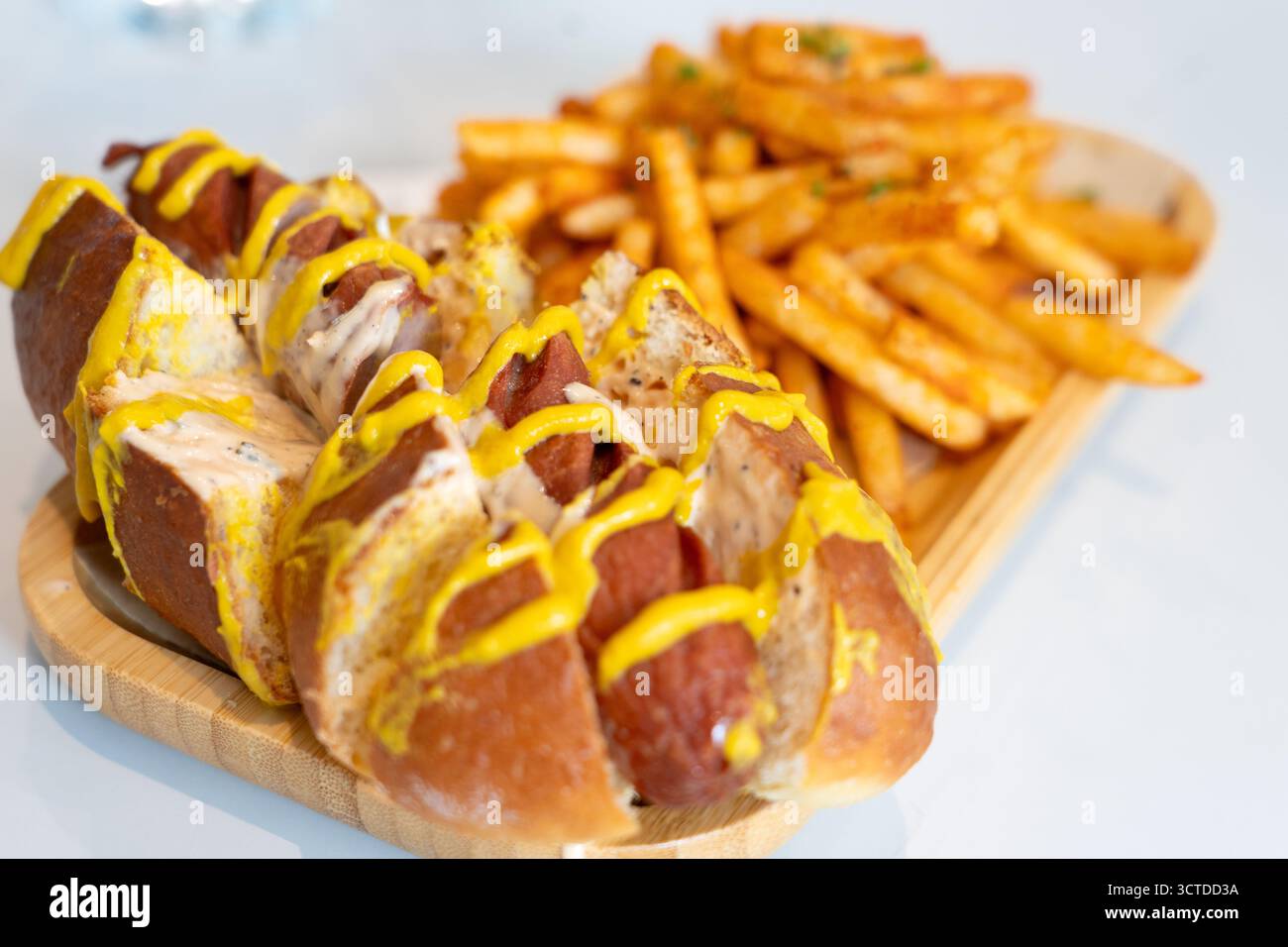 Hot dog caricati in soffici panini di pretzel con condimenti vivaci, serviti insieme a patatine fritte dorate per un pasto perfetto e appagante. Foto Stock