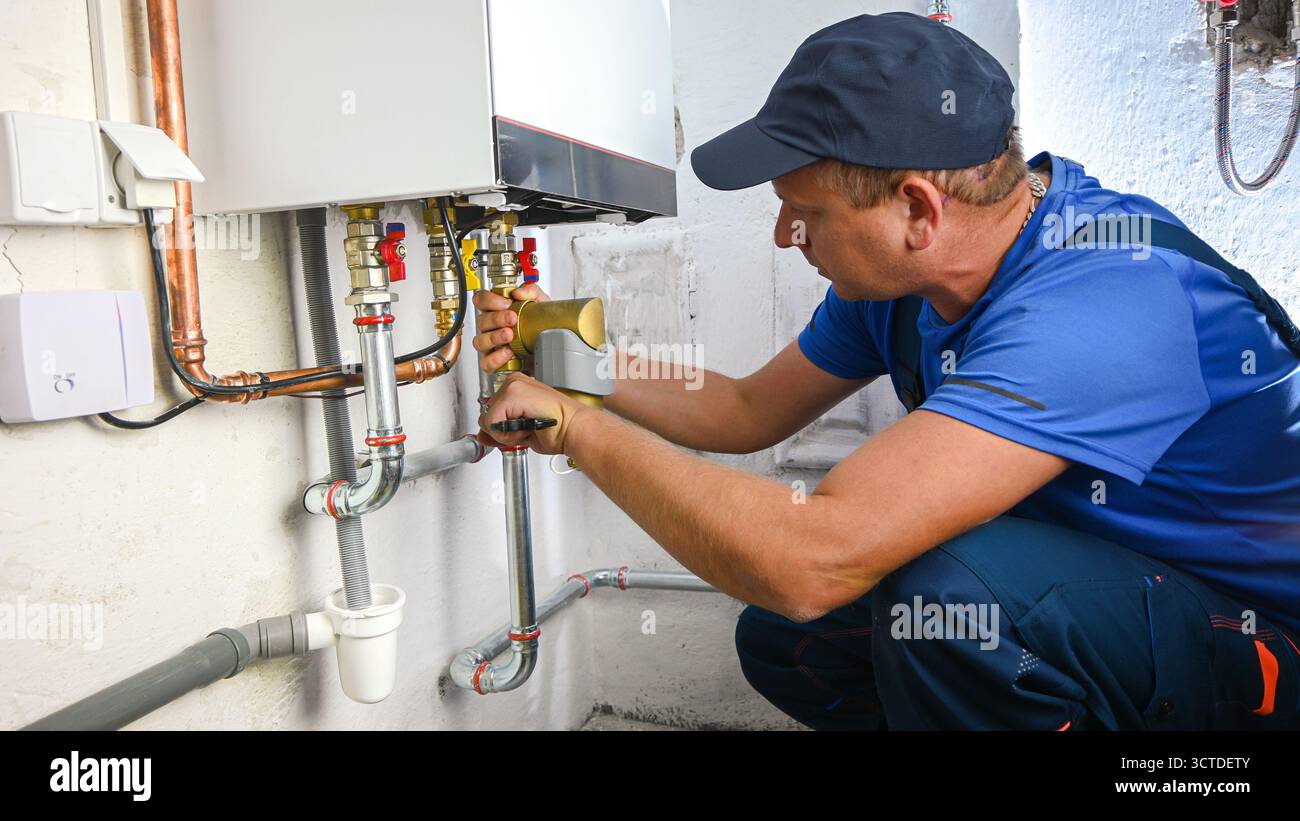 Idraulico che lavora su una caldaia, installando tubi di collegamento per un impianto di riscaldamento. Foto Stock