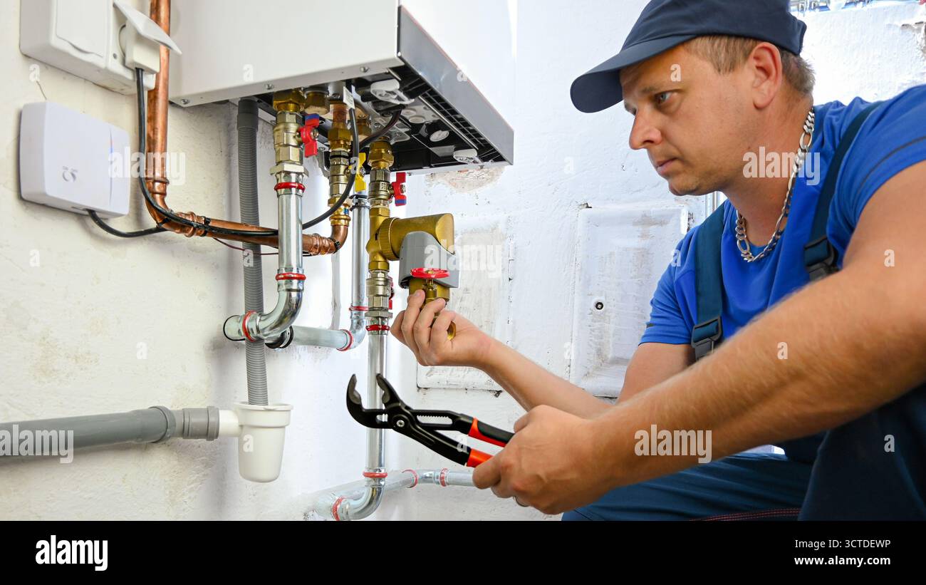 Idraulico che esegue la manutenzione e la riparazione di una moderna caldaia per riscaldamento domestico. Foto Stock