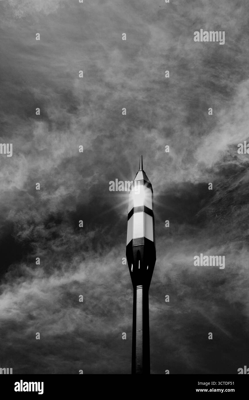Un'alta torre metallica illuminata dalla luce del sole contro le nuvole spettacolari, catturata in bianco e nero. Foto Stock