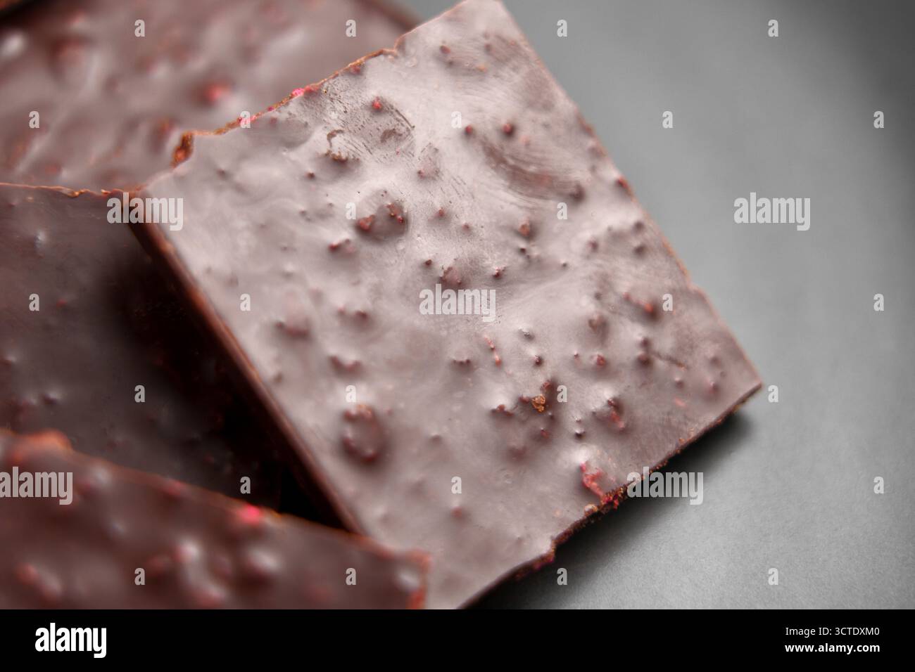 Quadrati di tavoletta di cioccolato fondente rotta con ripieno di fragole su un piatto di ceramica nera. Foto Stock