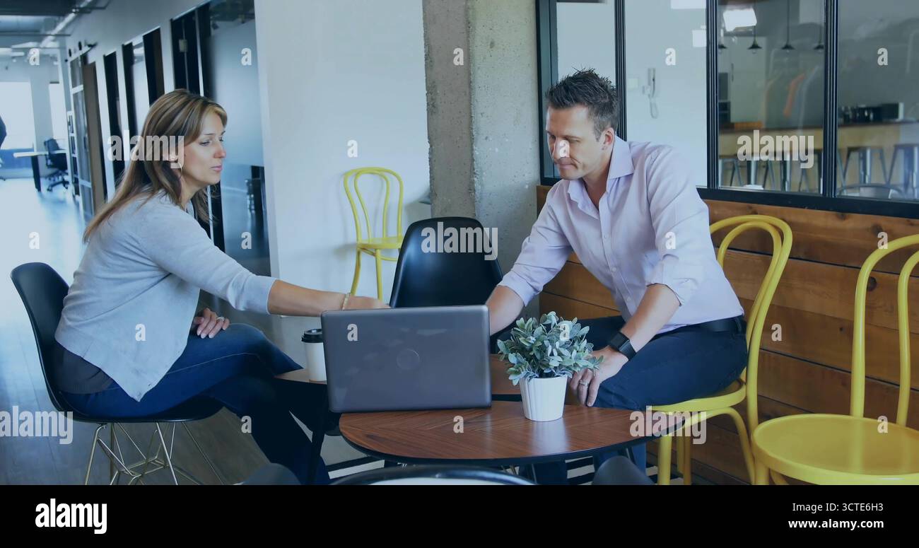 I colleghi si sono vestiti in modo informale nella sala dell'ufficio, con un computer portatile aperto, una tazza di caffè e una pianta in vaso Foto Stock
