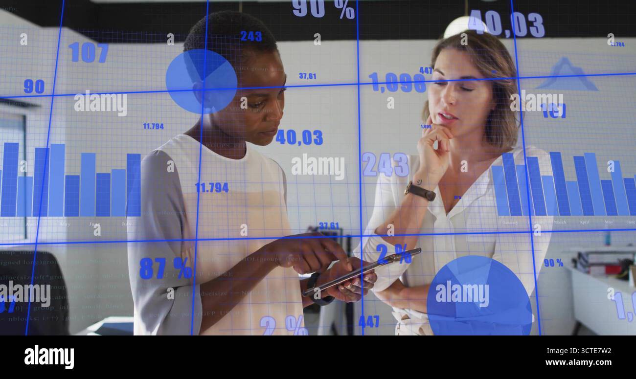 Esaminando un tablet, due donne aziendali analizzano i dati in un ufficio moderno con grafici fluttuanti Foto Stock