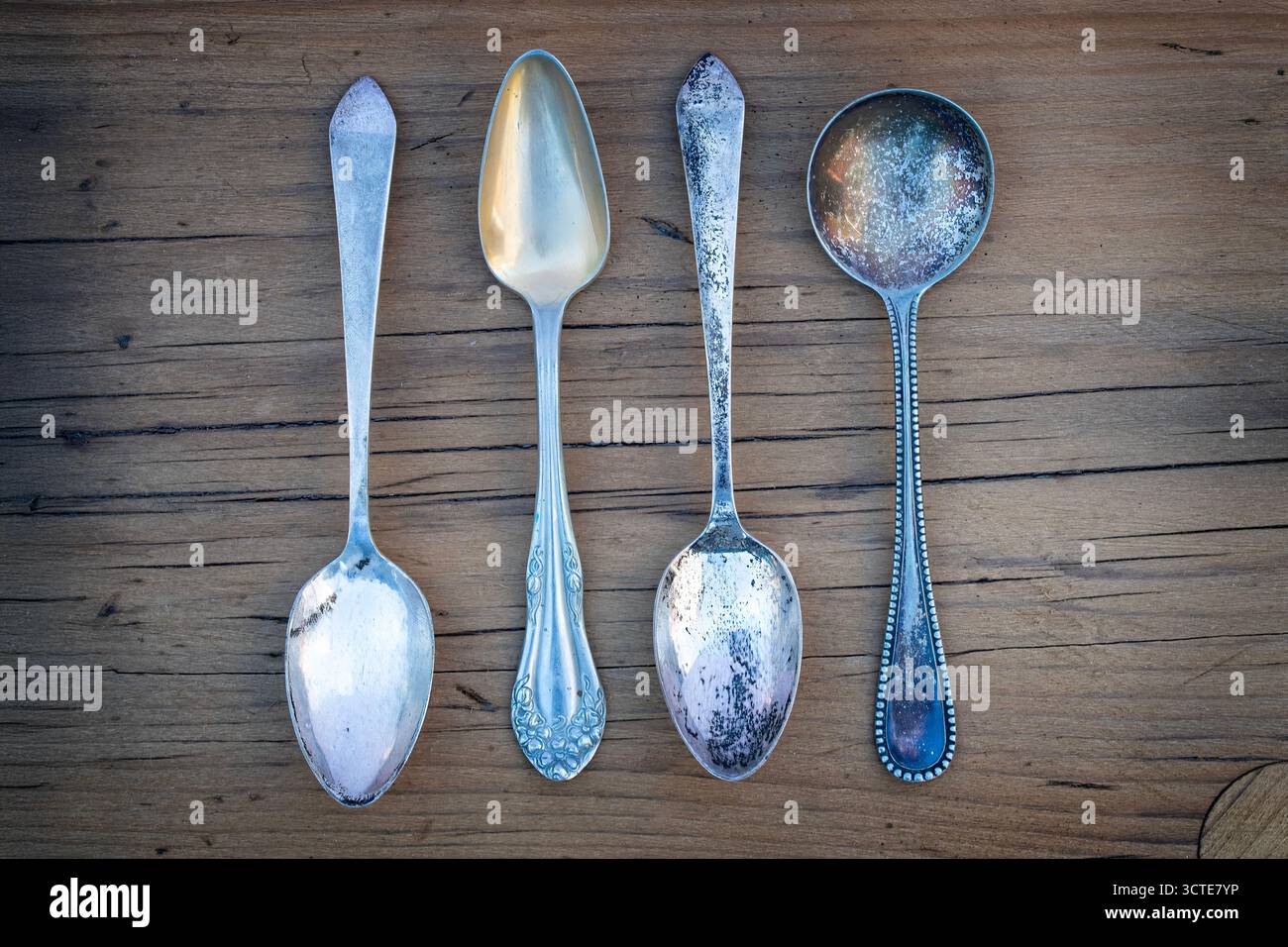 Quattro cucchiai d'argento antico su una vecchia tavola di legno Foto Stock