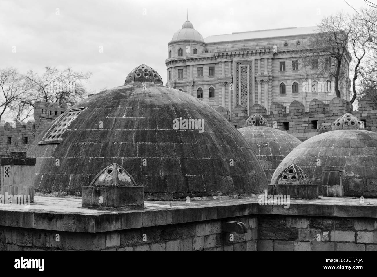 Baku, Azerbaigian. Vista sulla città vecchia. Fotografia monocromatica di cupole in pietra intemperie in un cortile della fortezza, con un grande edificio ornato che si erge dietro Foto Stock