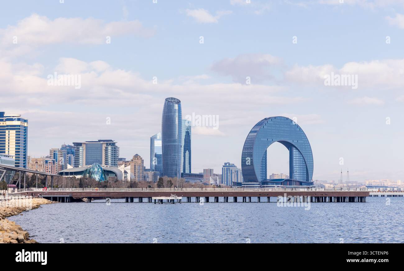 Un tranquillo paesaggio urbano sul lungomare caratterizzato da torri di vetro e da una caratteristica struttura ad arco circolare. Baku, Azerbaigian Foto Stock Un tranquillo paesaggio urbano sul lungomare caratterizzato da torri di vetro e da una caratteristica struttura ad arco circolare. Baku, Azerbaigian Foto Stock