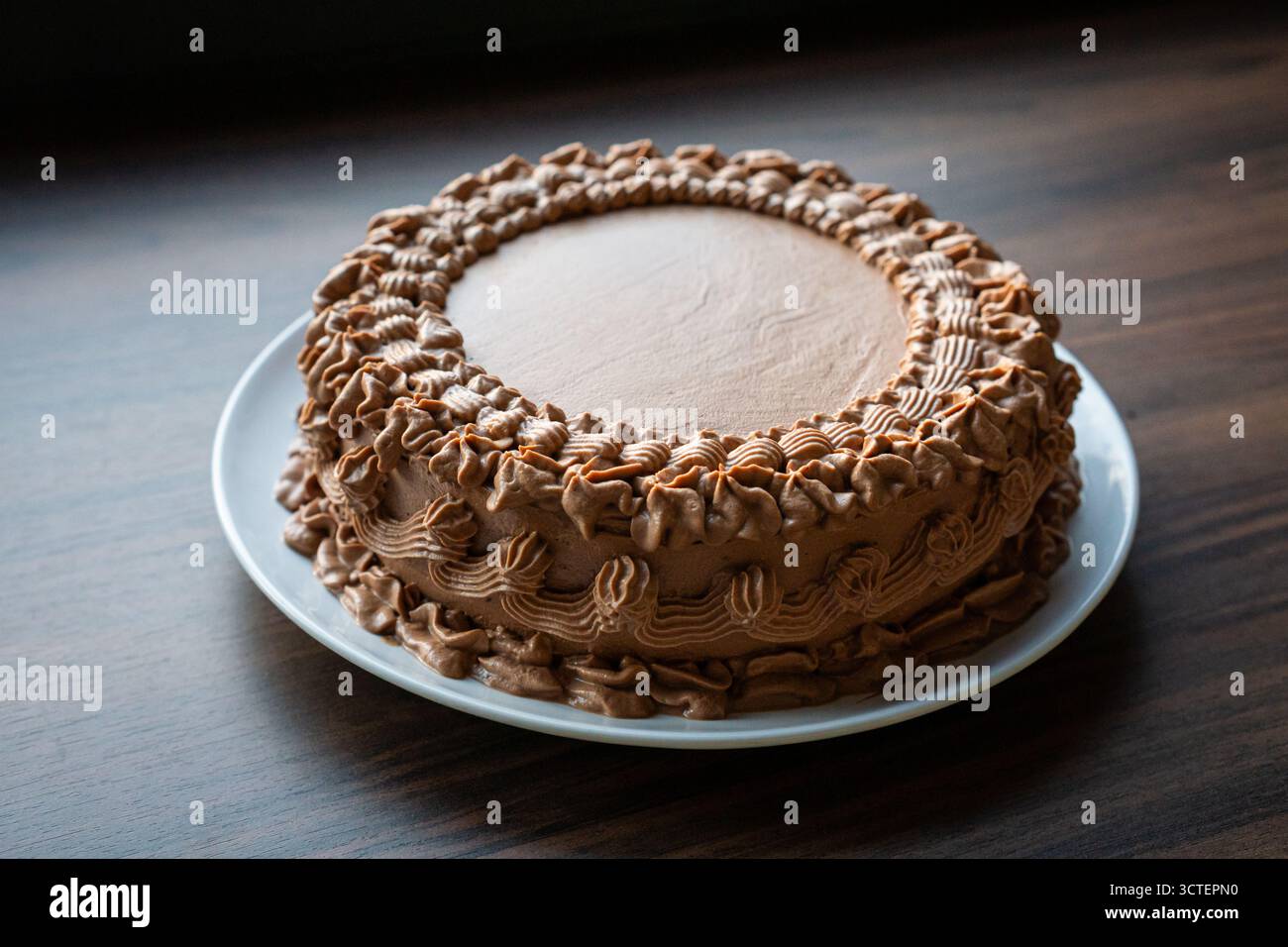 Primo piano di torta al cioccolato con decorazione crema su piatto bianco su un tavolo di legno con luce soffusa, perfetto per i concetti di panificazione e dessert. Foto Stock