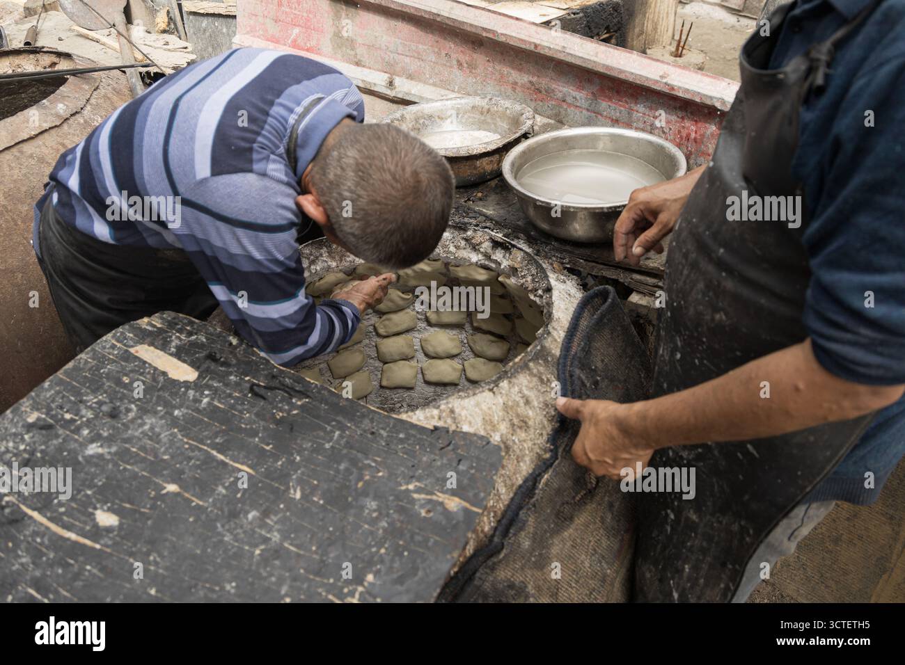 Kashgar, Cina - 07 settembre 2025: Vista dei fornai che sistemano meticolosamente l'impasto all'interno di un forno tandoor, le loro mani si muovono con precisione praticata in mezzo al calore e alla tradizione. Foto Stock