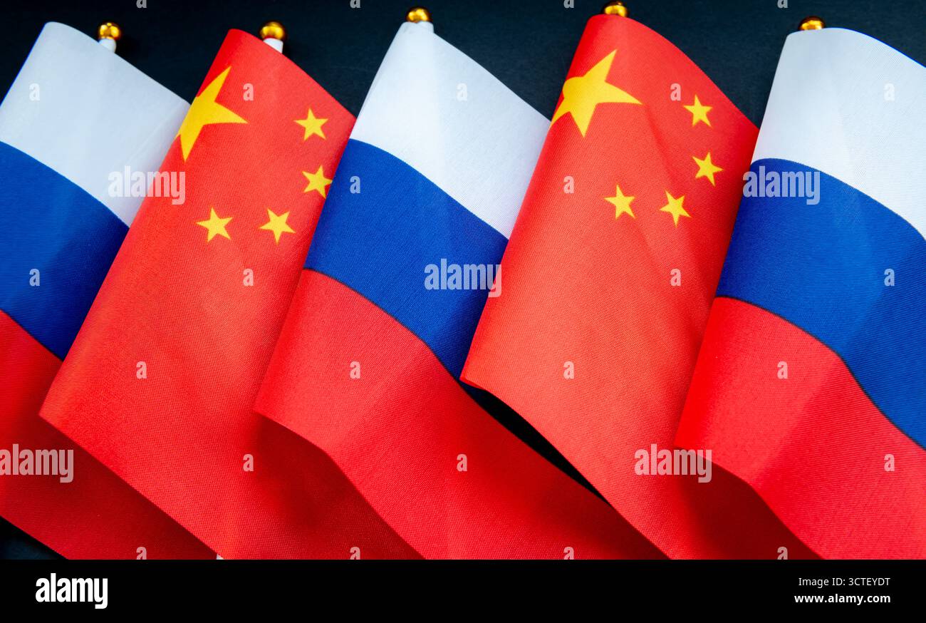 Una fila di bandiere nazionali cinesi e russe su pali di bandiera con sfondo nero. Un concetto di relazioni tra Russia e Cina. Foto Stock