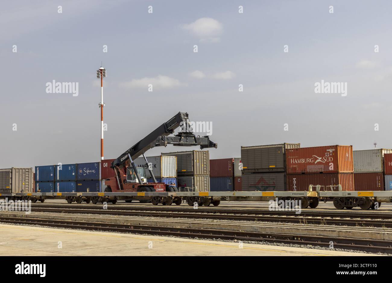 Suswa, Kenya - 5 agosto 2025: Vista di un treno che trasporta container di merci, accostato a un cielo limpido, con una torre rossa e bianca alta. Foto Stock