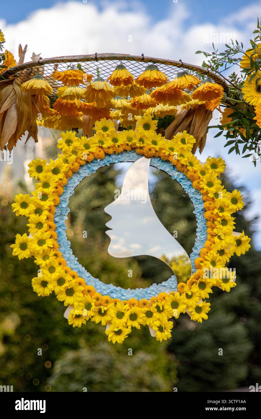 Uno specchio decorativo a forma di volto femminile, all'interno di un cerchio di fiori gialli autunnali, crisantemi, in occasione di un festival autunnale Foto Stock