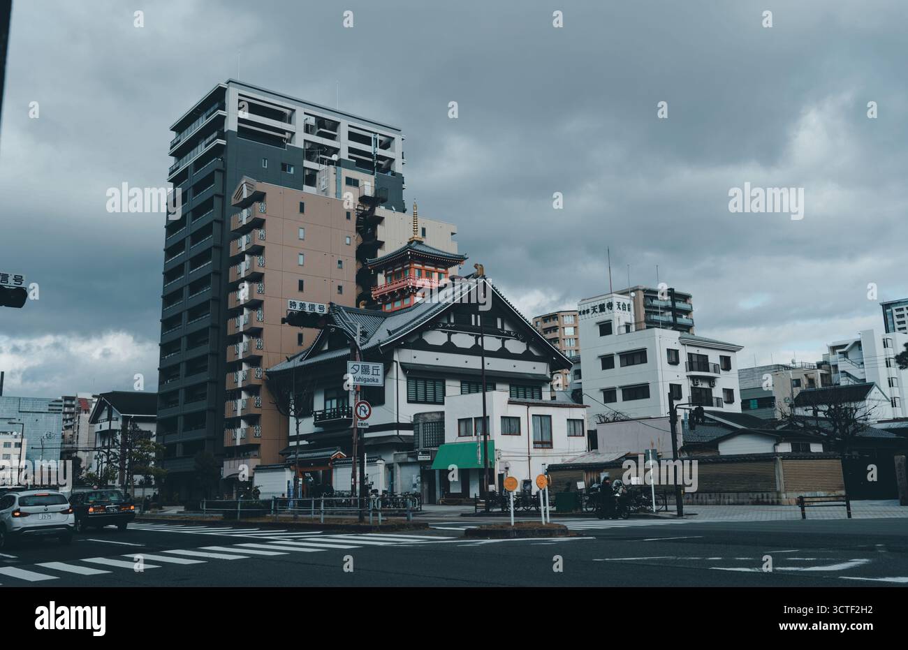 Una tradizionale struttura giapponese sorge in un trafficato incrocio di Osaka, incorniciata da edifici moderni sotto pesanti nuvole Foto Stock