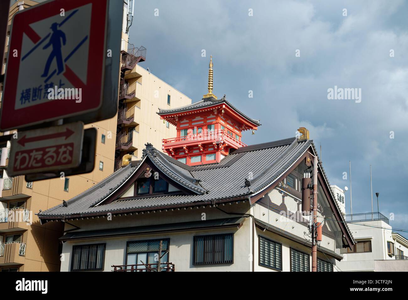 Una pagoda rossa sorge da un edificio tradizionale di Osaka, incorniciato da un'architettura moderna e da un cartello stradale in primo piano Foto Stock