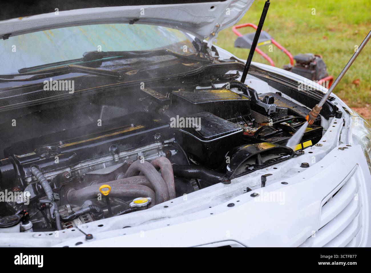 Il vapore fuoriesce dal motore dell'auto che viene pulito con un'idropulitrice in un garage all'aperto Foto Stock